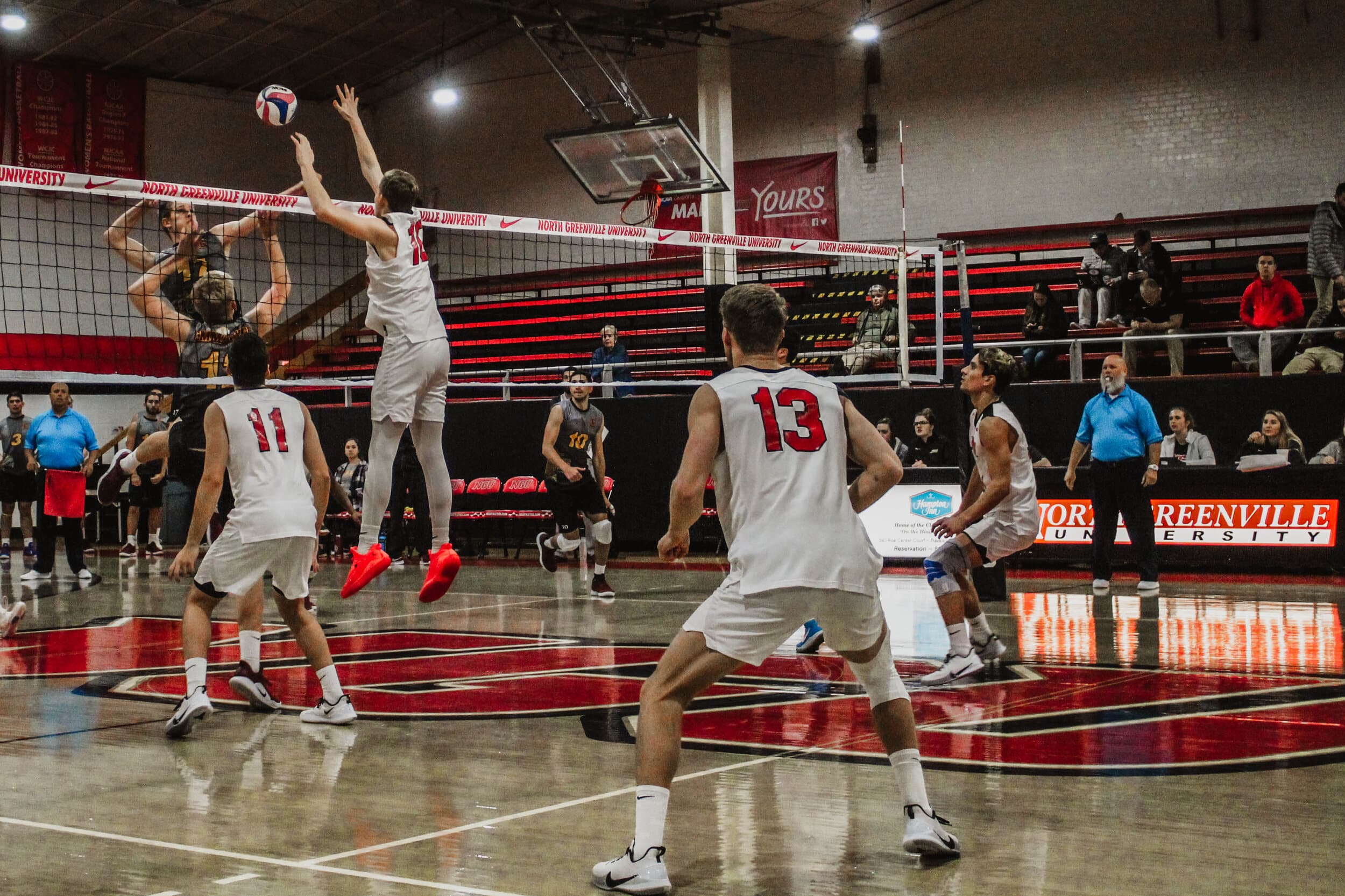 As an Emmanuel player jumps to spike the ball, junior Brandon Baker (10) leaps to block the hit.