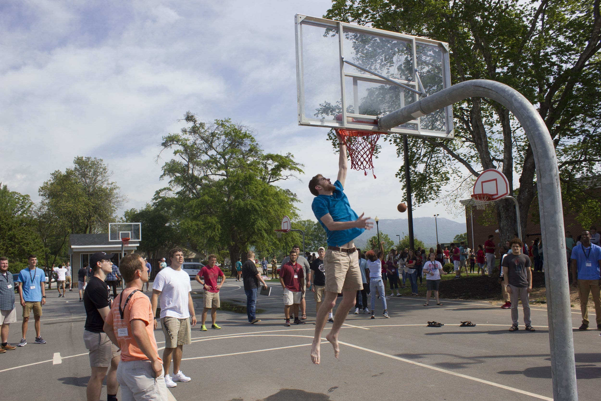 A few guys mingle and watch as others show off their basketball skills.