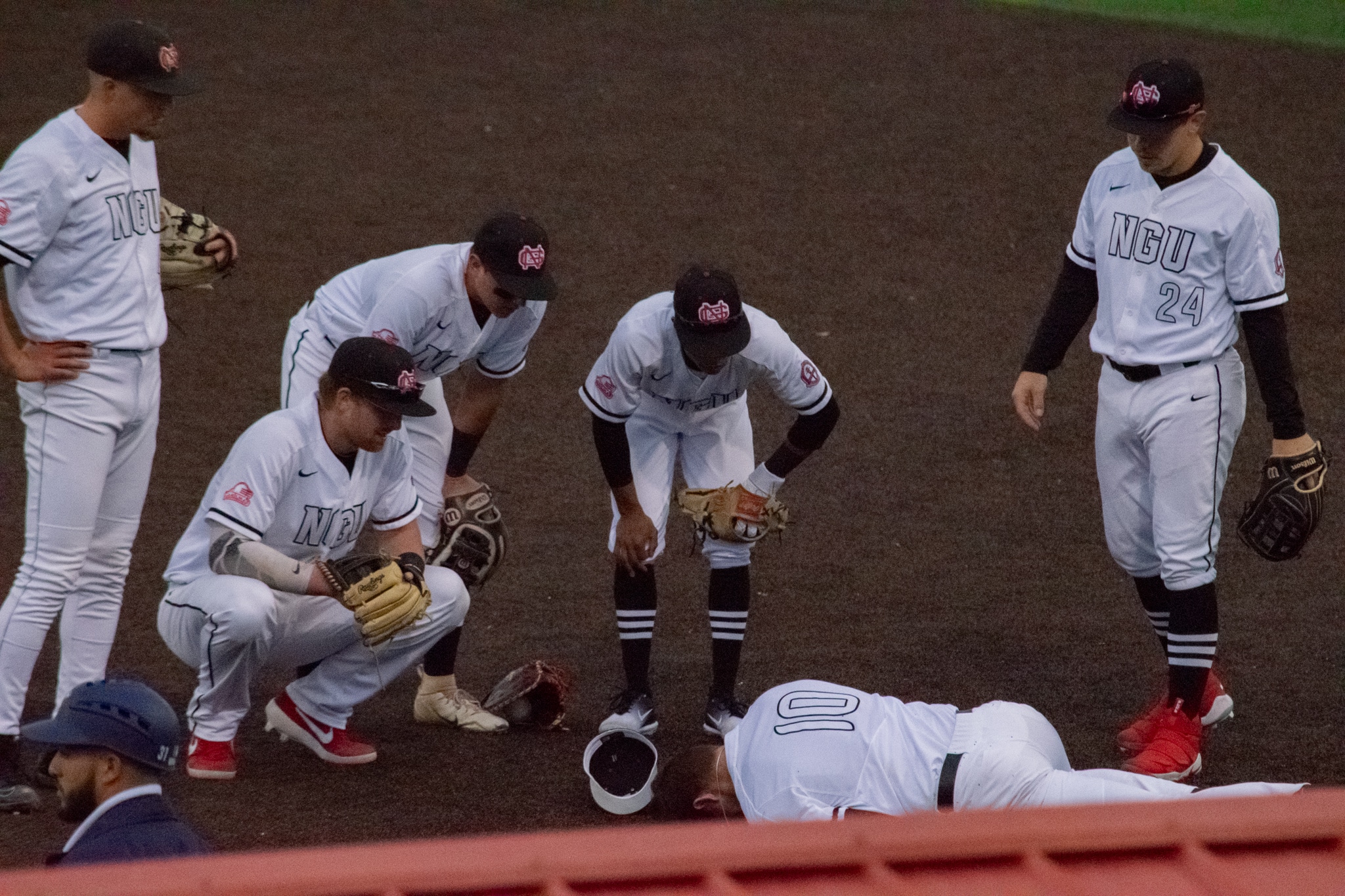 While trying to catch the ball on first, Sasser (10) is run over by his opponent and is injured. He is surrounded by his teammates as they await the trainer to get to him.