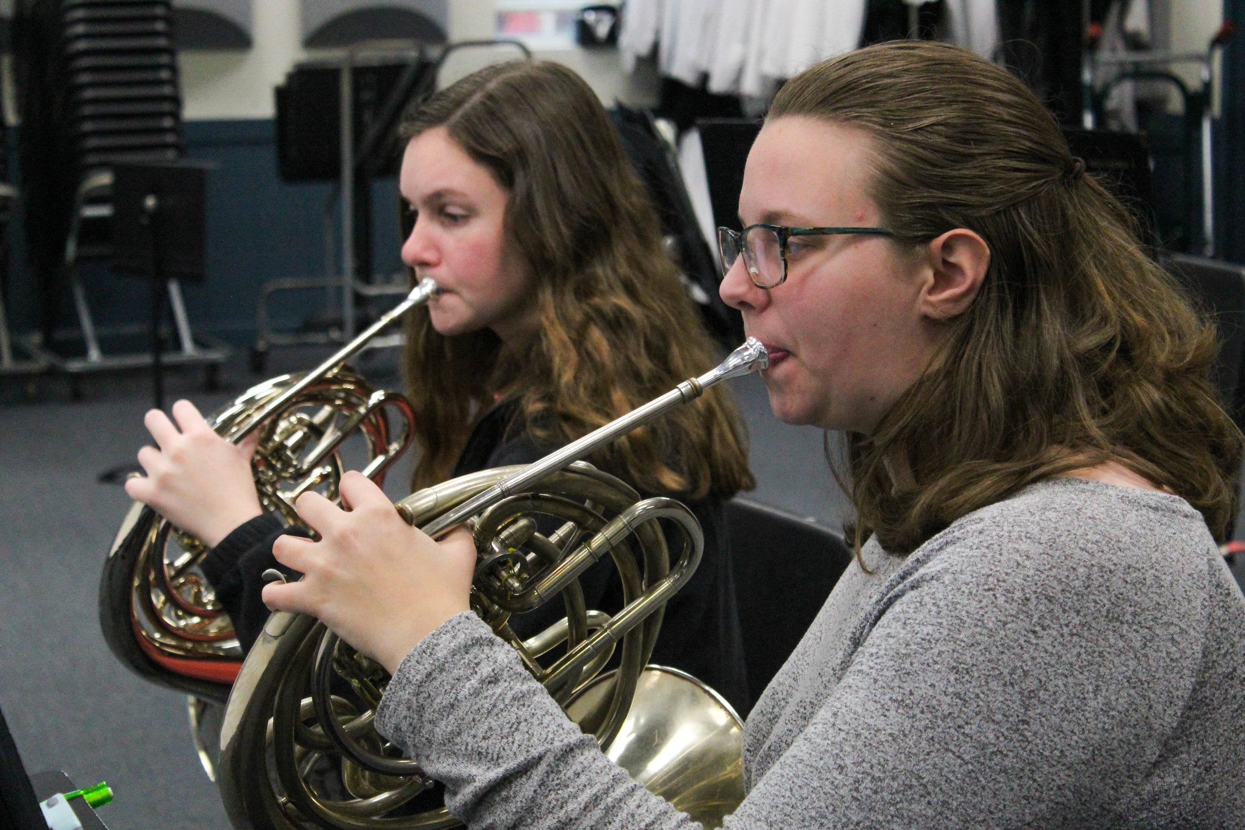 The two orchestra students practice playing their horns.