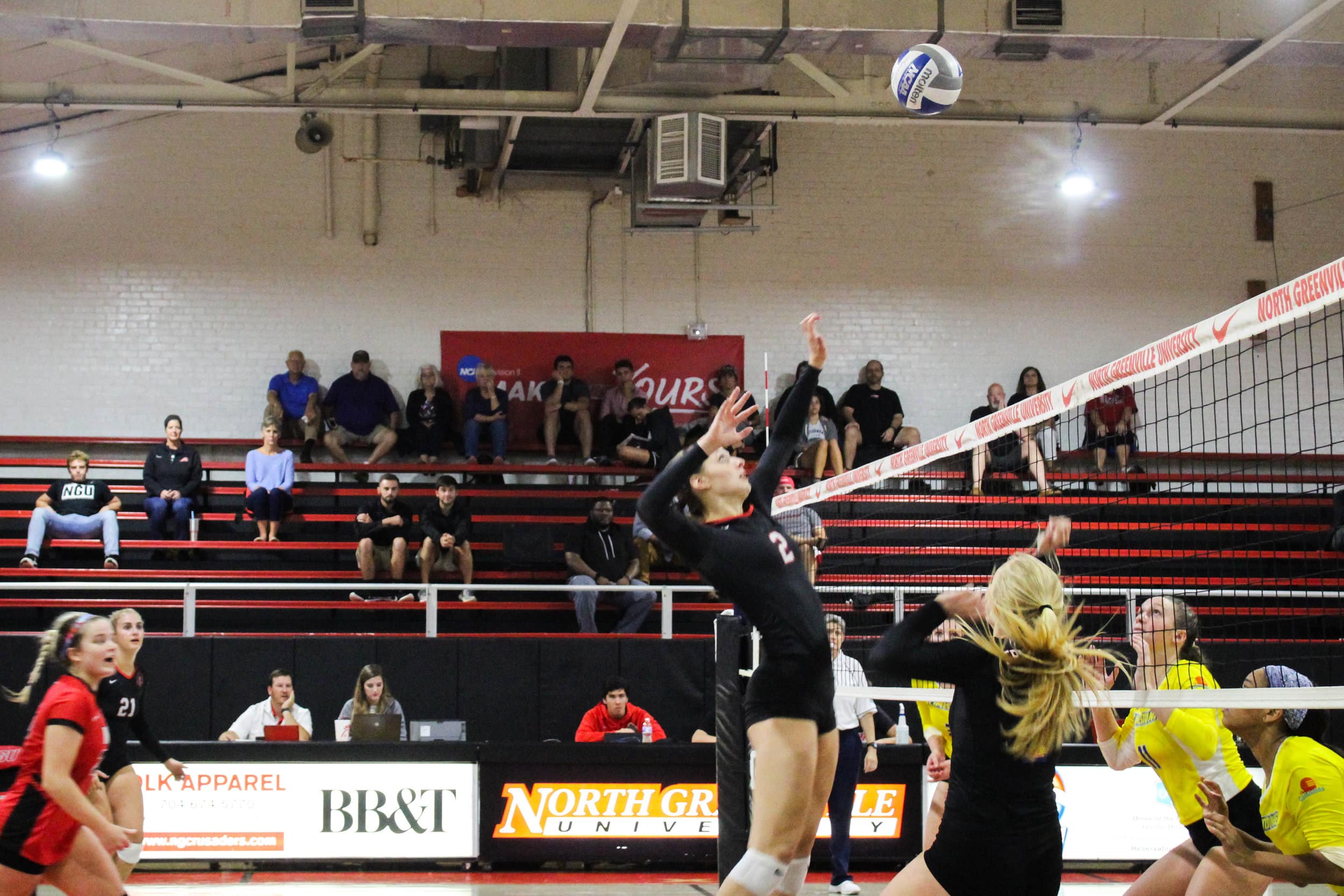 Freshman Paige Beisecker (2) spikes the ball over the net while two Limestone players squat preparing for the spike.