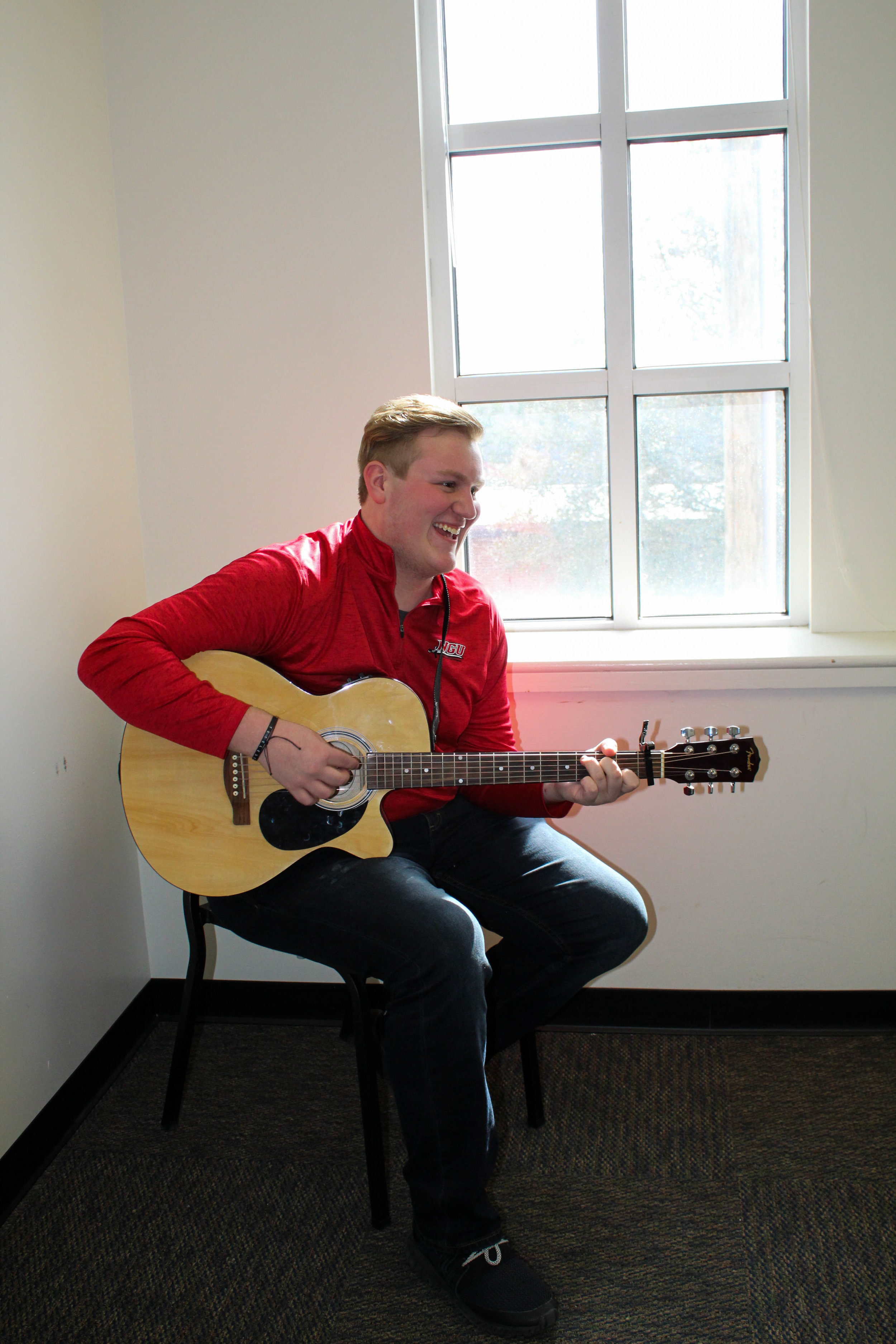 Nicolas Olson, a freshman double major in business administration and Christian studies, practices his guitar as he wears red for the awareness of heart disease.