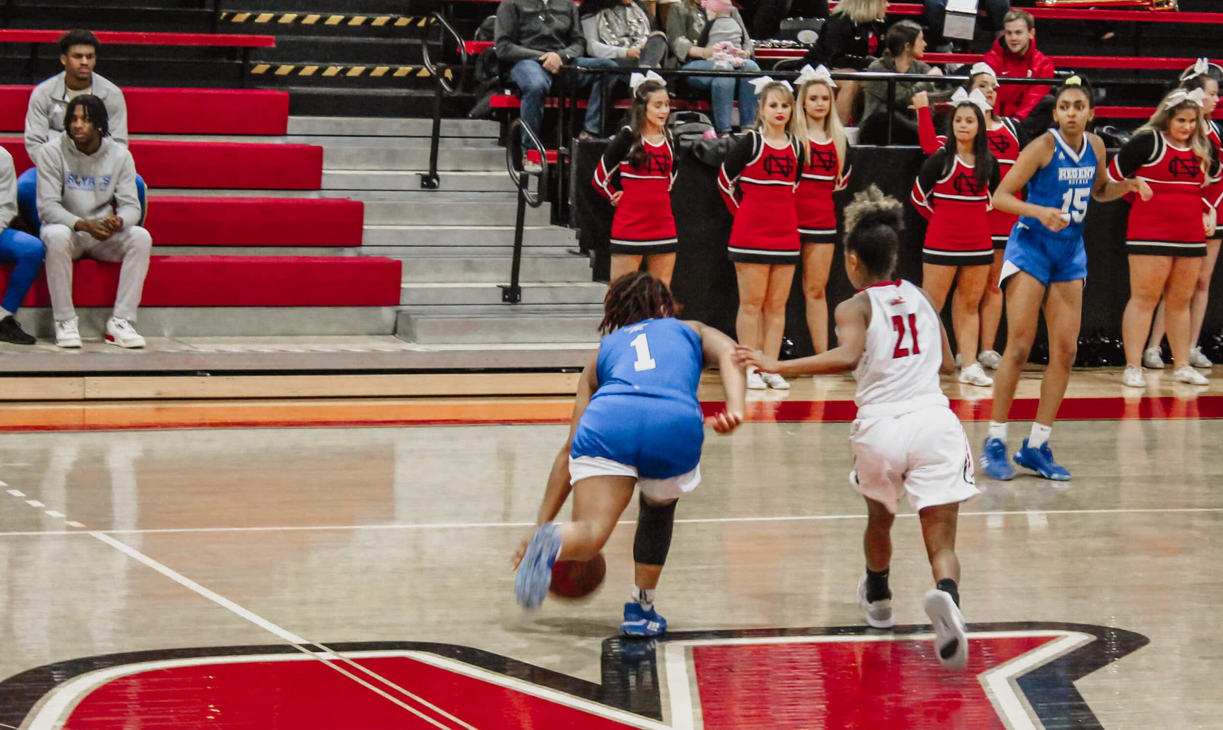 Junior point guard Savannah Hughes (21) guards a Regent player as she dribbles down the court.