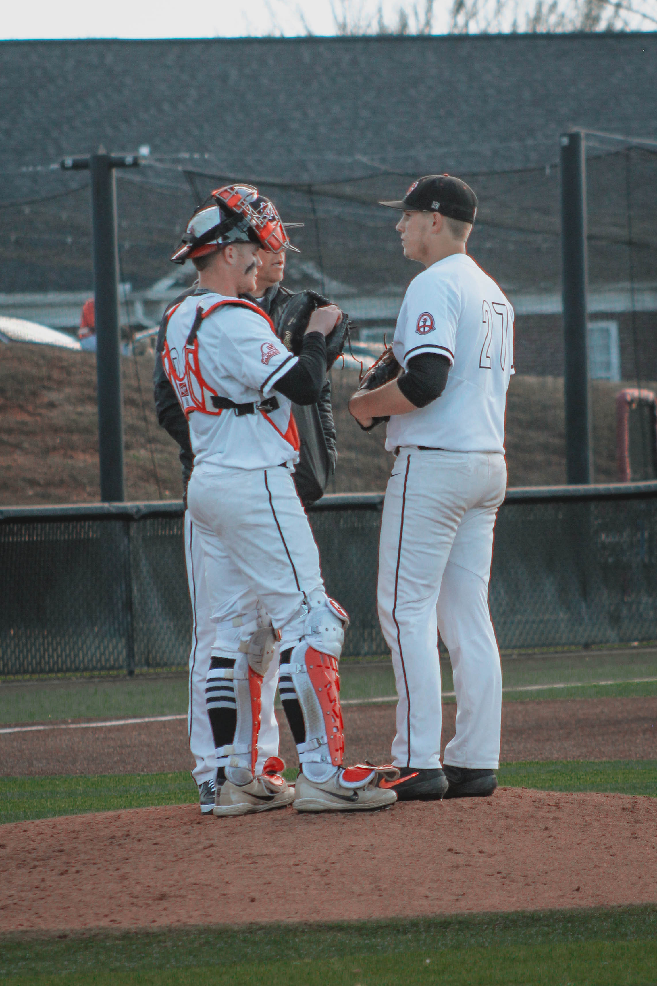 The catcher (23), pitcher (27) and a coach talk on the pitchers mound.