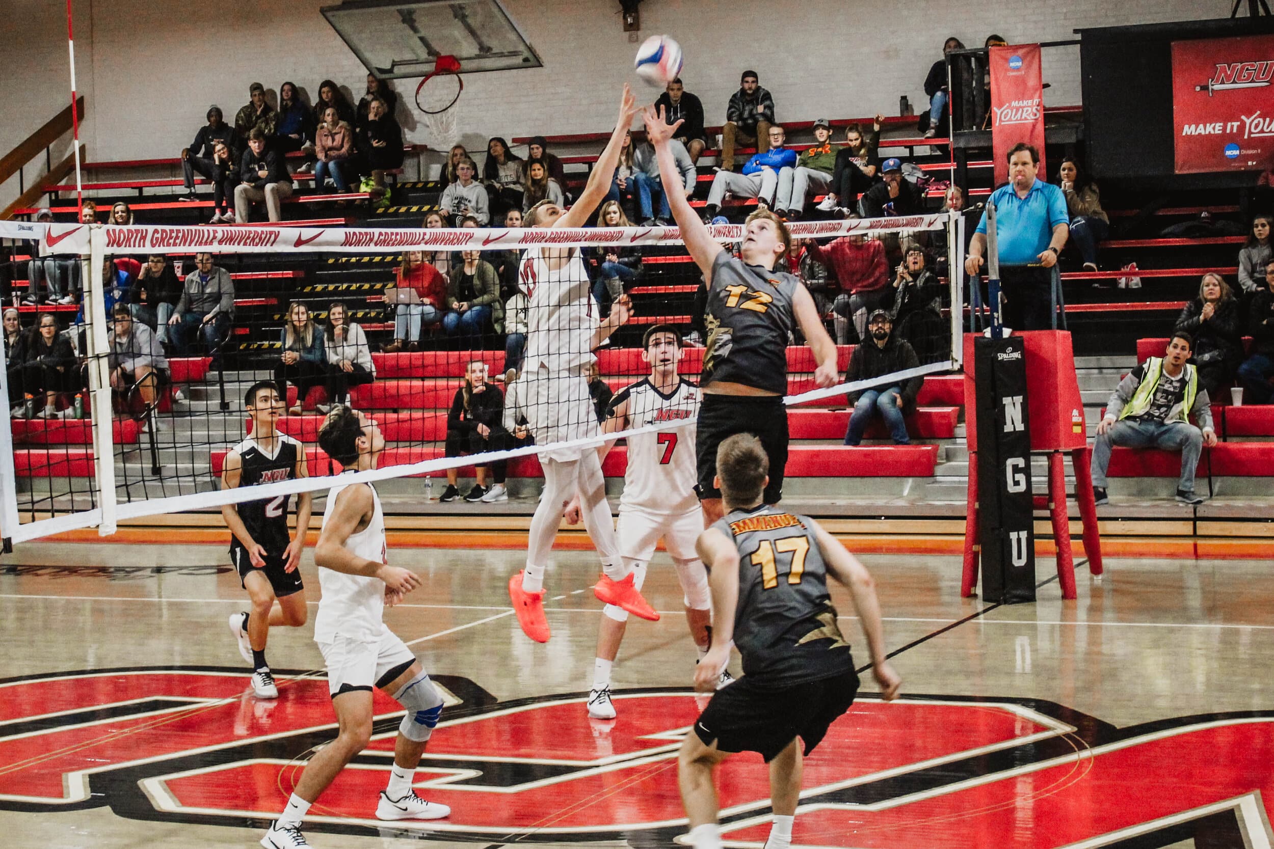 Brandon Baker (10), a junior, and an Emmanuel player both jump attempting to hit the ball over the net to their opponents side.