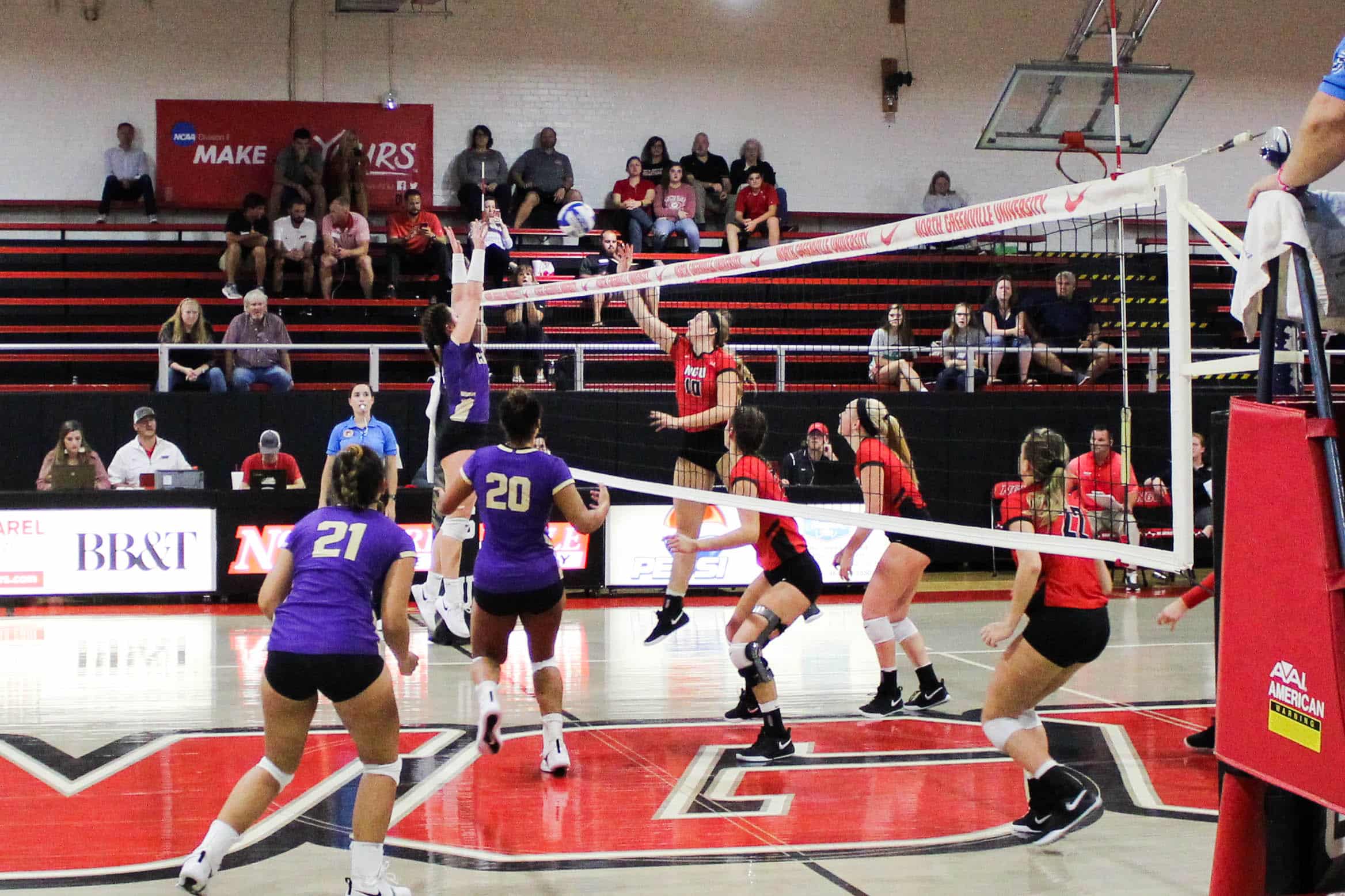 Freshman, Catherine Lant (10) leaps as she hits the ball back while a player jumps on the other side of the net to block.