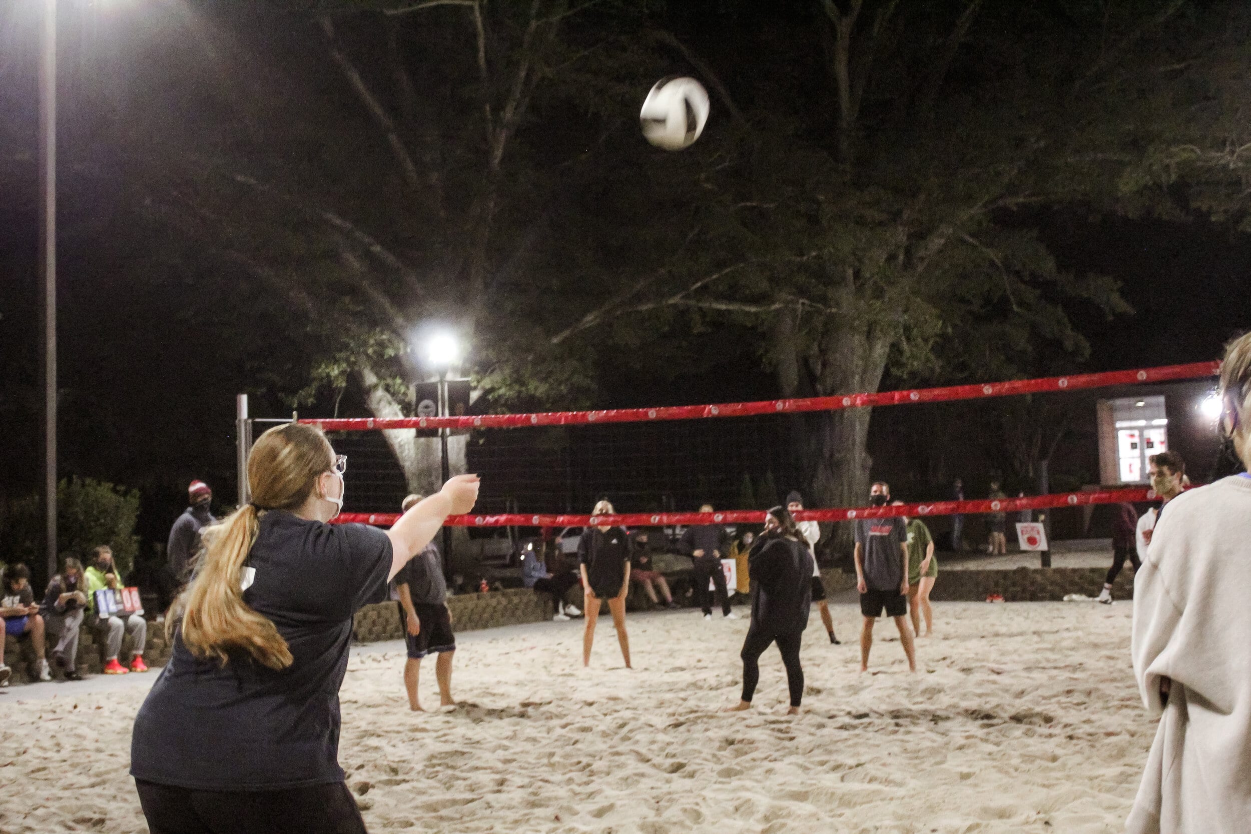 As the ball is served over the net, members of both teams are watching and ready to play the pass.