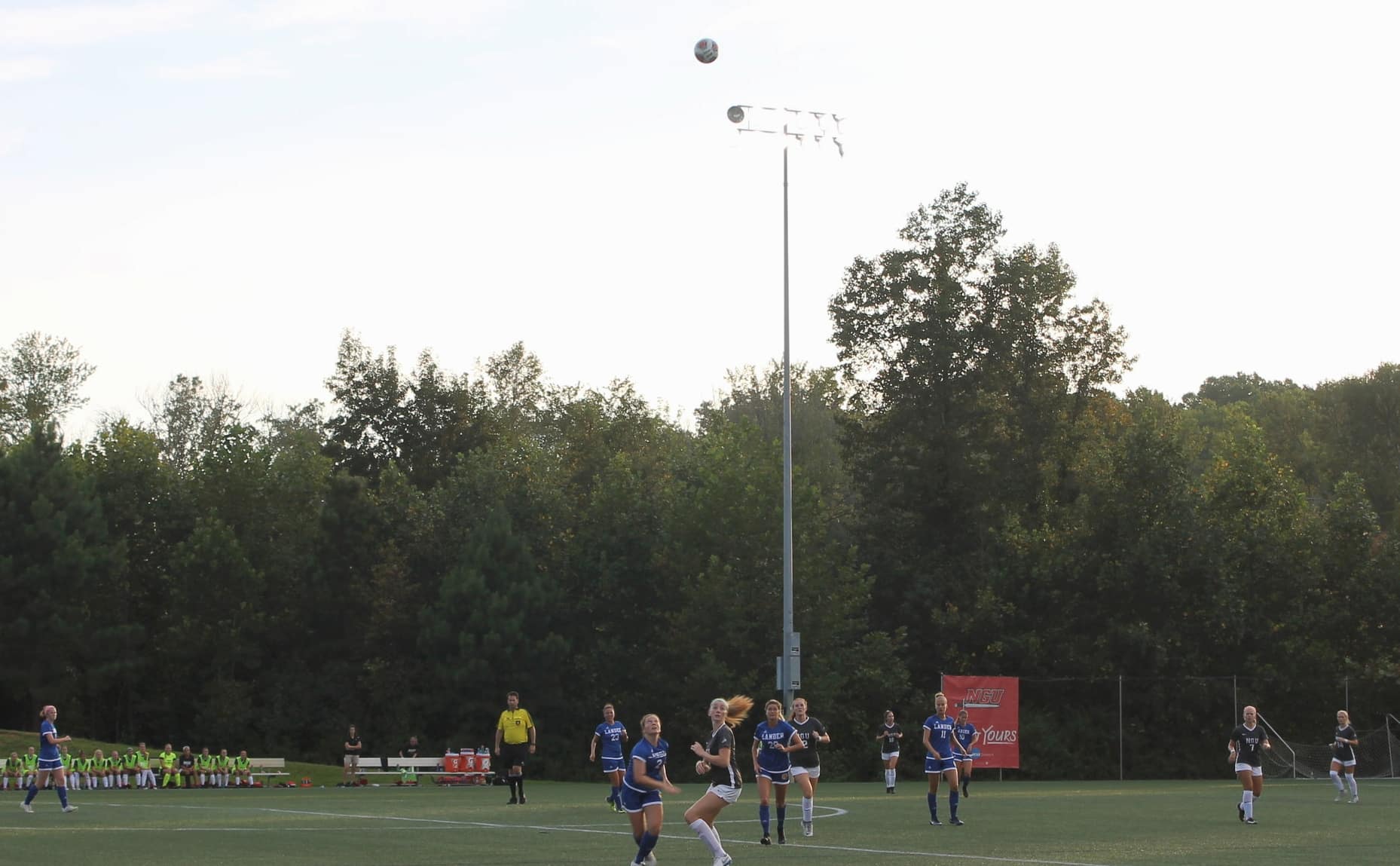 NGU and Lander university chasing after a ball after it had been juggled in the air by many diferent players on opposing teams.