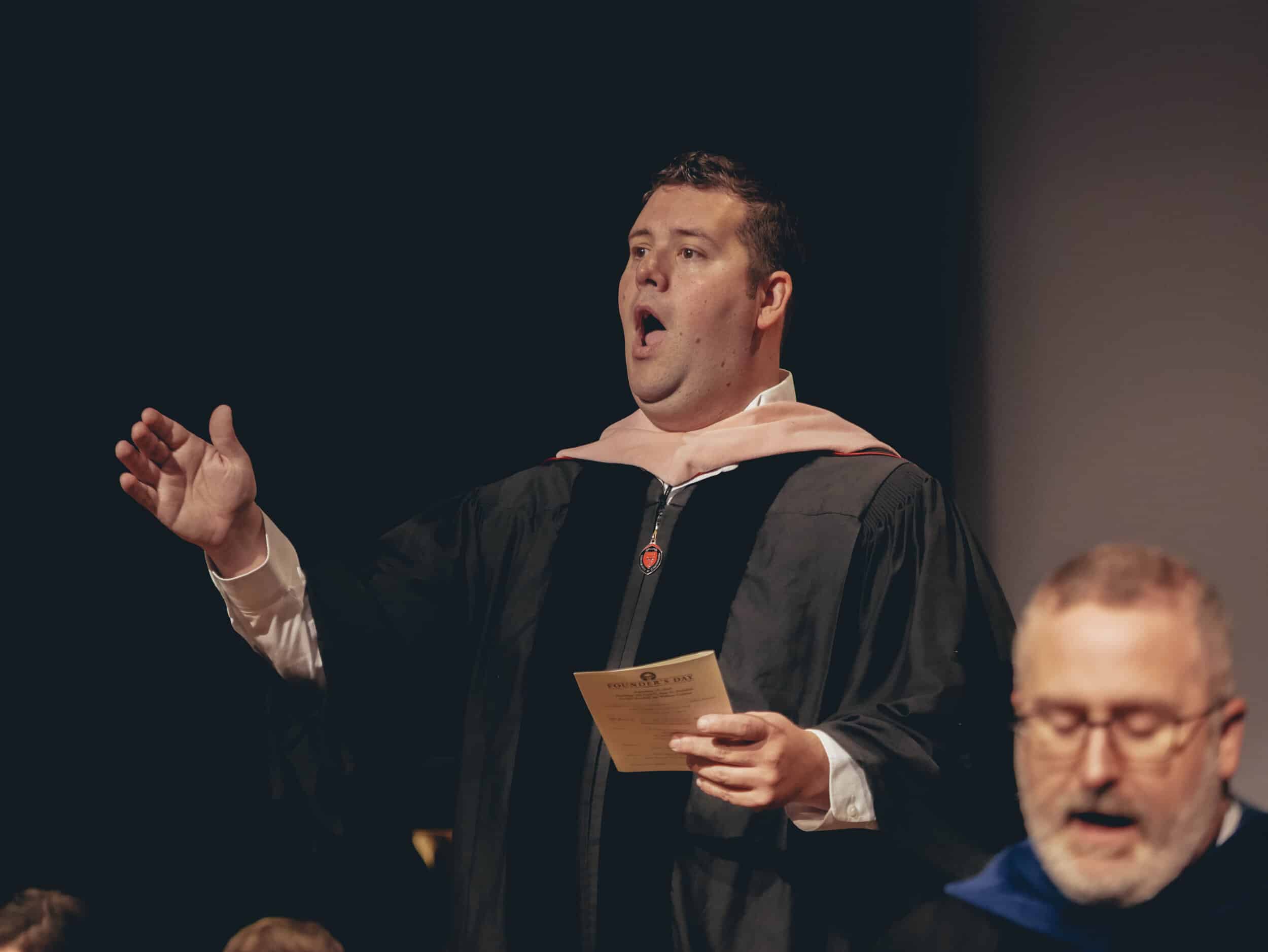 Seth Killen associate professor of voice leads the congregation in the reciting of the universities alma mater.